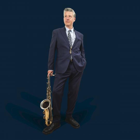 un homme en costume debout avec un saxo