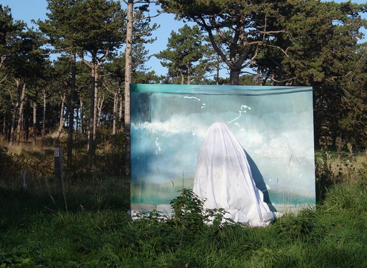 photo d'une  grand peinture bleu clair avec une personnes couverte d'un drap blanc dans une forêt de pins