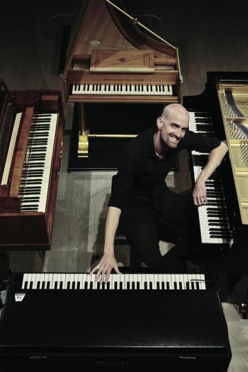 affiche d'un homme chauve et barbu au milieu de plusieurs claviers piano, synthétiseur, clavecin 