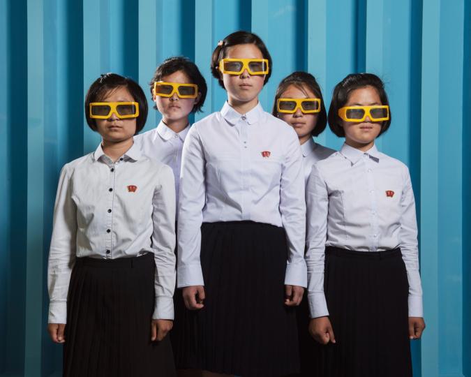 photo de cinq jeunes filles asiatiques avec uniforme blanc et noir avec lunettes de soleil jaunes devant un mur tôle bleu