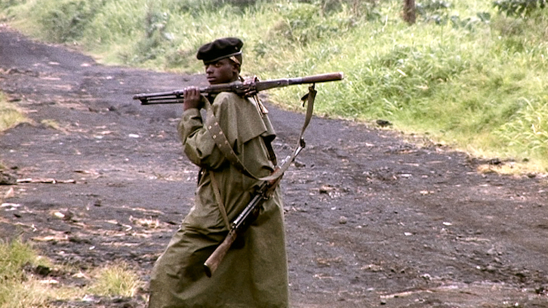 photo d'un militaire noir de profil avec berret  et long manteau kaki et fusil sur l'épaule en bandoulière sur un chemin de terre