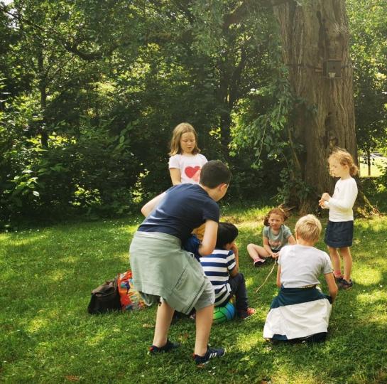 photo d'un groupe d'enfants debout et assis sur une pelouse/parc devant des arbres