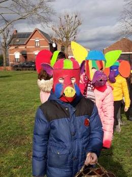 groupe d'enfants en file avec un masque se carnaval et un tambour dans une prairie