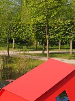 Photo d'un parc avec une marre - étang  et une maison rouge en métal qui coule