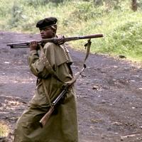 photo d'un militaire noir de profil avec berret  et long manteau kaki et fusil sur l'épaule en bandoulière sur un chemin de terre